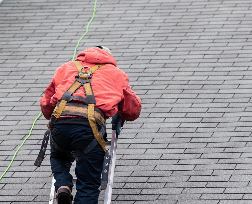 Back View Of A Man In Protective Gear Climbing A Ladder To Get Onto A Roof