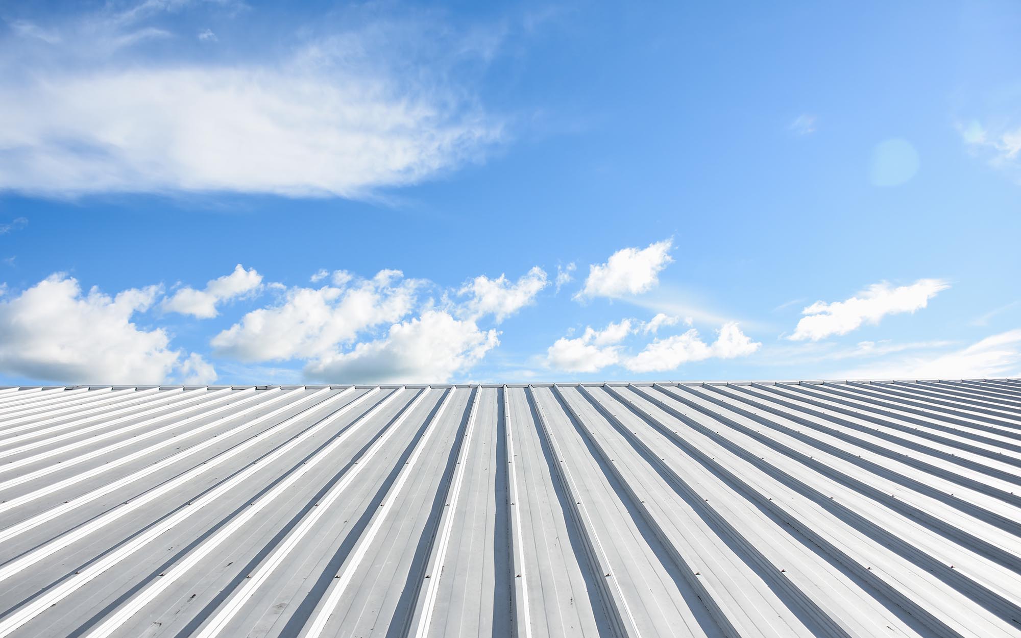 Front view of a white commercial roof against a partly cloudy sky Front View Of A White Commercial Roof Against A Partly Cloudy Sky