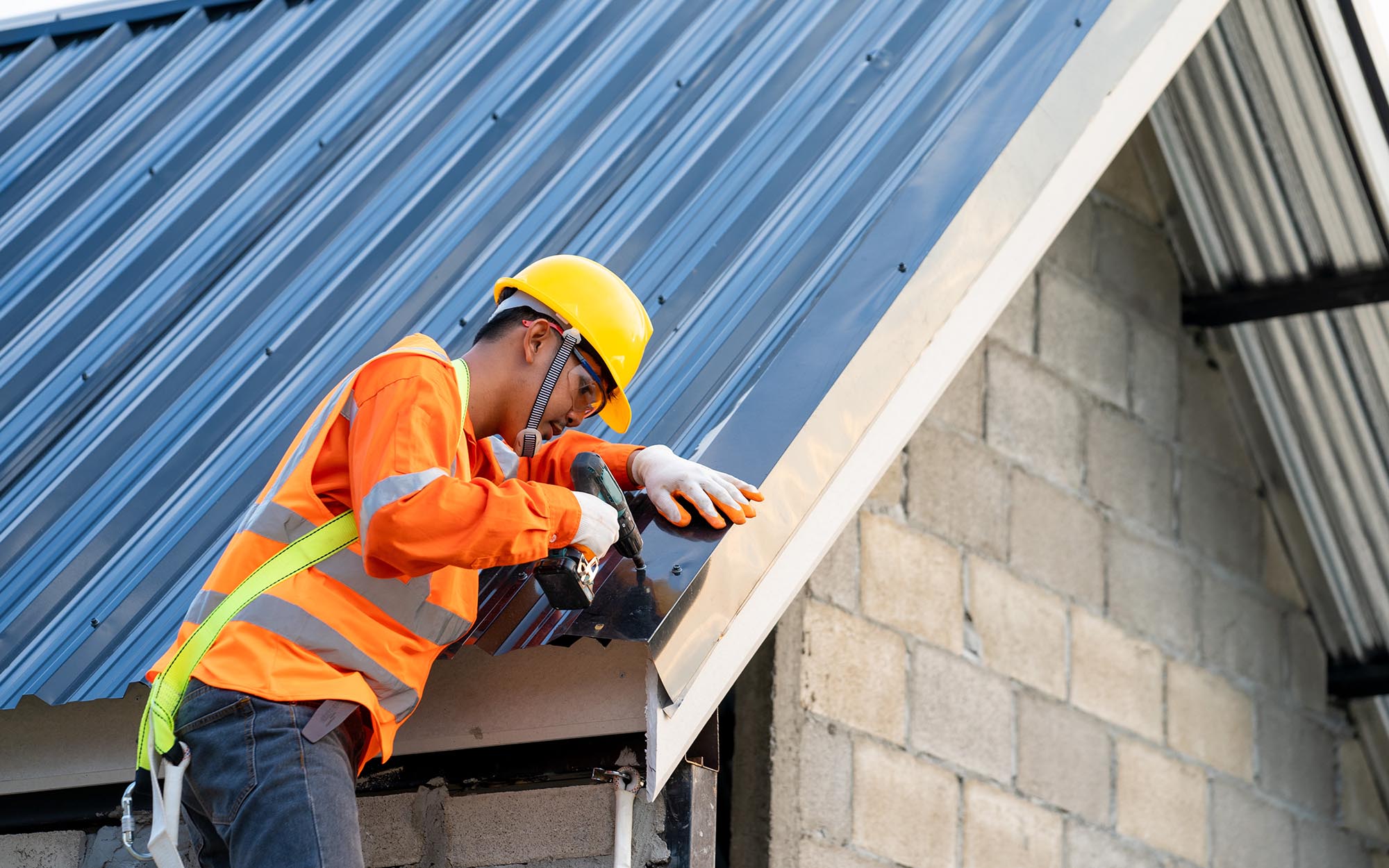 Side View Of A Man In Protective Gear Drilling Metal Roofing